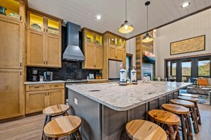 A modern kitchen with wooden cabinets, a large island with stools, and a view to the outside. - Splash Villa (Pigeon Forge)