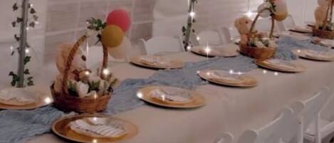 A tented dining area with white chairs, tables set with plates, and decorative elements like balloons and baskets.