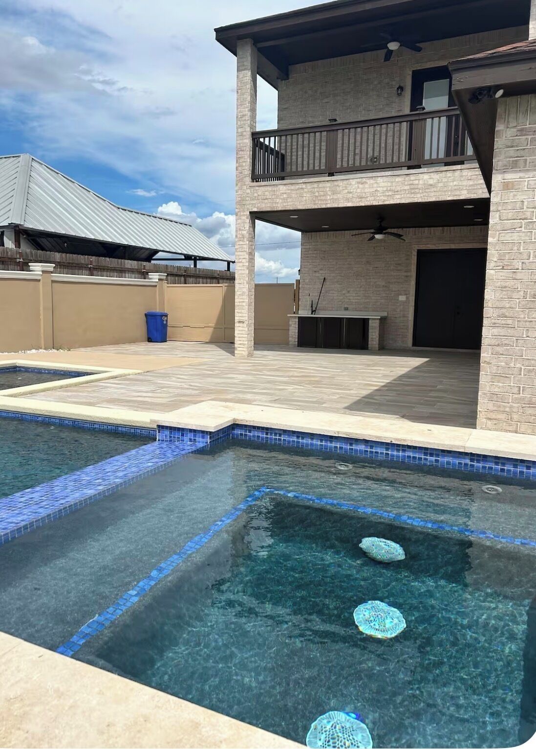 Ein Schwimmbecken mit klarem Wasser, eine überdachte Terrasse und ein zweistöckiges Gebäude mit Balkon.