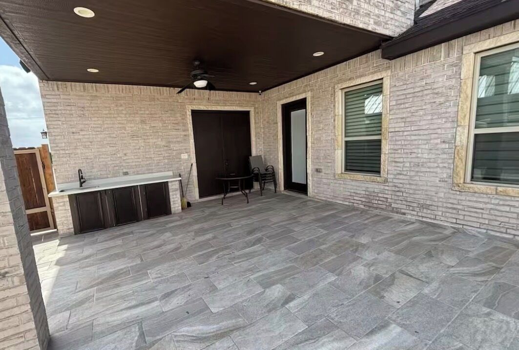 Eine überdachte Terrasse mit Steinboden, einer integrierten Bar und einem Deckenventilator.