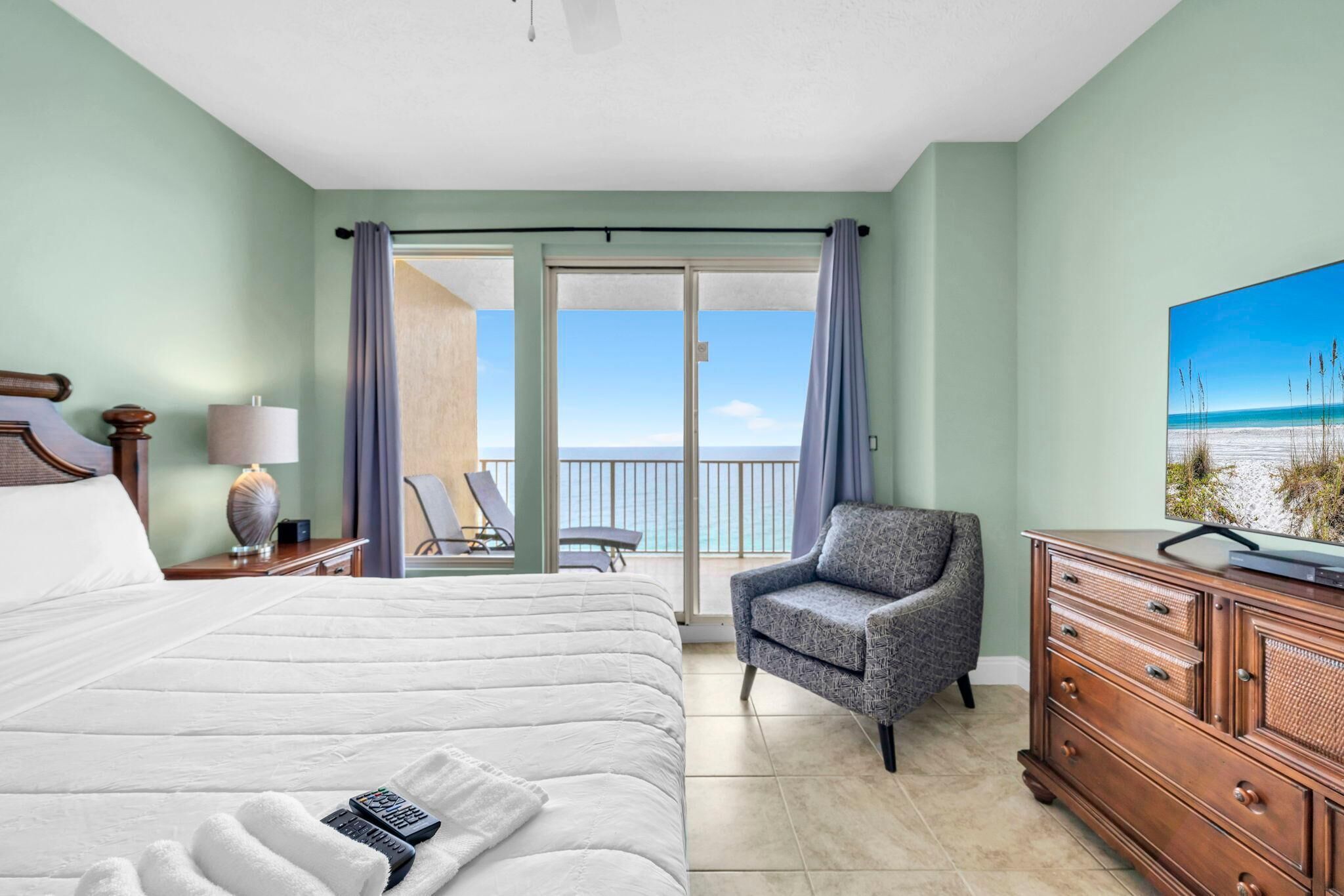 Habitación de hotel con cama, una silla, cómoda y balcón con vista al océano.
