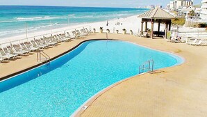 Una piscina de borde curvo junto a una playa con sillones de descanso y un pabellón.