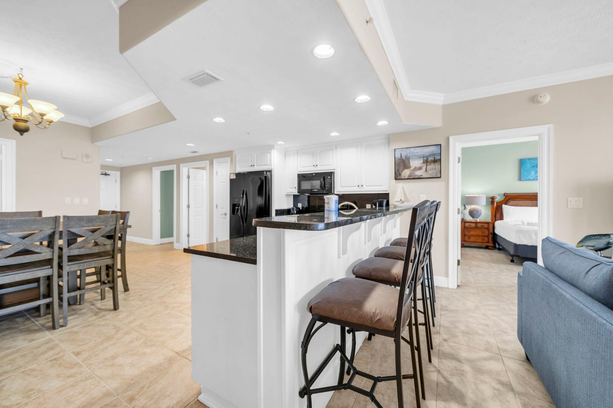 A spacious kitchen with white cabinets, a central island with bar stools, and a dining area with a wooden table and chairs.