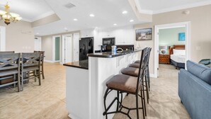 Una cocina amplia con armarios blancos, una isla central con taburetes y un comedor con mesa y sillas de madera.