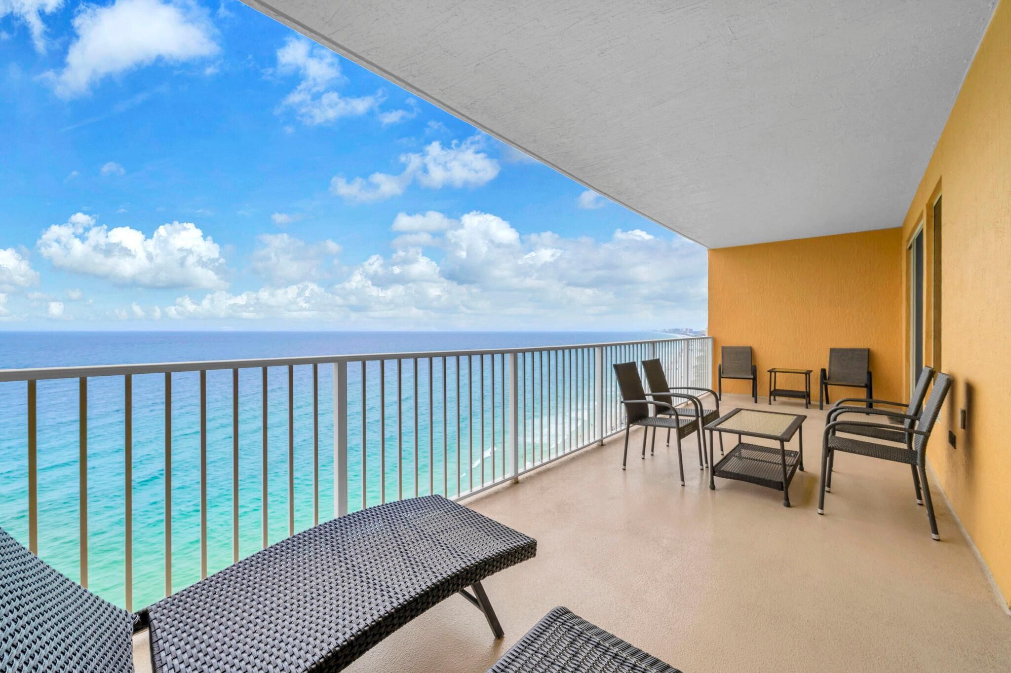 A balcony with a view of the ocean, a table with chairs, and a sofa.
