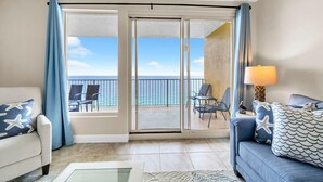 Habitación con sofá, sillón, lámpara y vista al océano a través de una puerta corrediza.