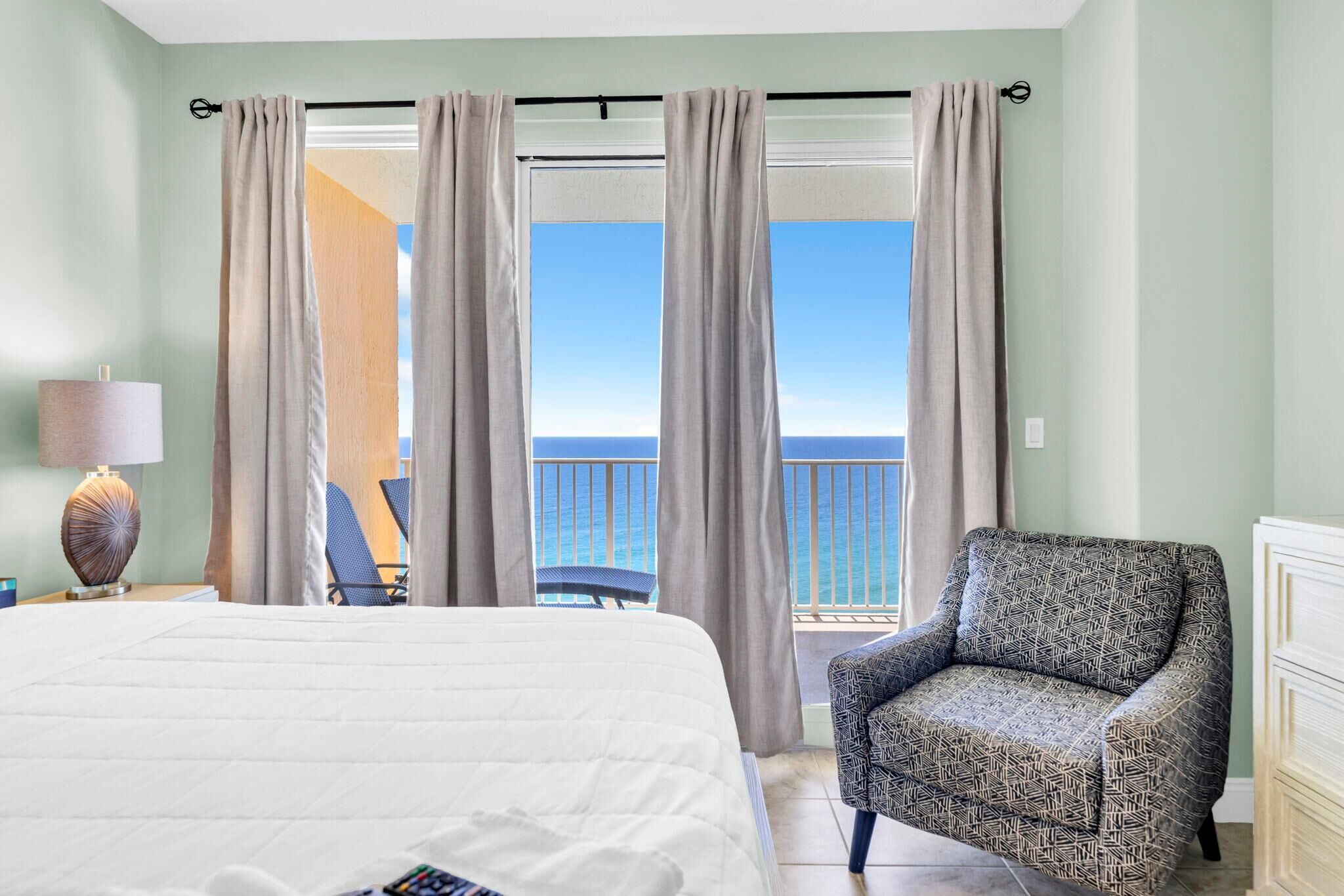 A hotel room with a bed, a chair, a lamp, and a view of the ocean.