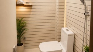 Un baño moderno con inodoro, ducha y lavamanos. Hay plantas y artículos de aseo en estantes.