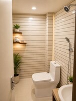 A modern bathroom with a toilet, a shower, and a sink. There are plants and toiletries on shelves.