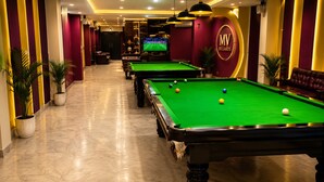 Una sala de billar con varias mesas de billar, el logotipo de billiards y una pantalla de televisión al fondo.