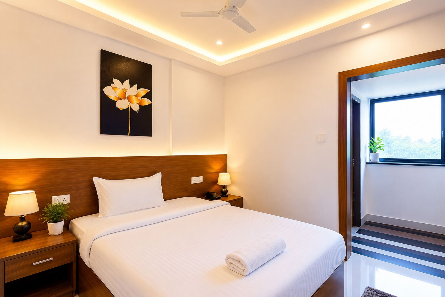 Une chambre d’hôtel avec un lit, des tables de chevet, des lampes, un ventilateur de plafond, une fenêtre et une plante.