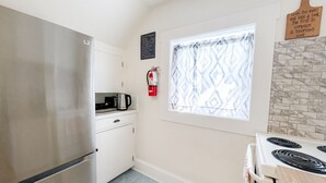Una cocina compacta con un refrigerador de acero inoxidable, una estufa y una ventana con cortinas estampadas.