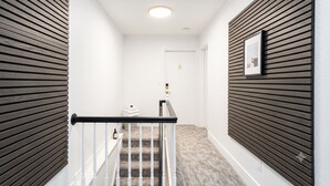 Un pasillo moderno con una escalera, paneles de madera en las paredes y una puerta con número.