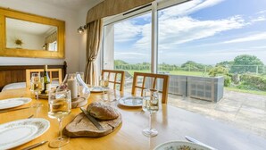 A dining table set with plates, glasses, and a bread loaf, overlooking a scenic landscape. - Swn y Mor Bach - sleeps 6 guests  in 3 bedrooms (Criccieth)