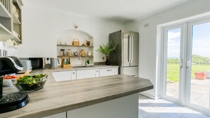 A modern kitchen with white cabinets, a stainless steel refrigerator, and a large window. - Swn y Mor Bach - sleeps 6 guests  in 3 bedrooms (Criccieth)
