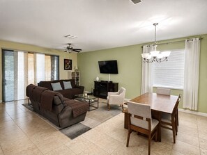 A living room with a sofa, coffee table, TV, and dining area with chairs and a table. - Tampa Sunshine Oasis / Heated Saltwater Pool / 4Bed, 3Bath / Sleeps 10 / Fenced (Tampa)