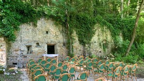 Un mur de pierre avec une petite ouverture, entouré de chaises vertes et d’une table.