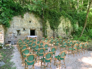 Un mur de pierre avec une petite ouverture, entourĂ© de chaises vertes et dâune table.