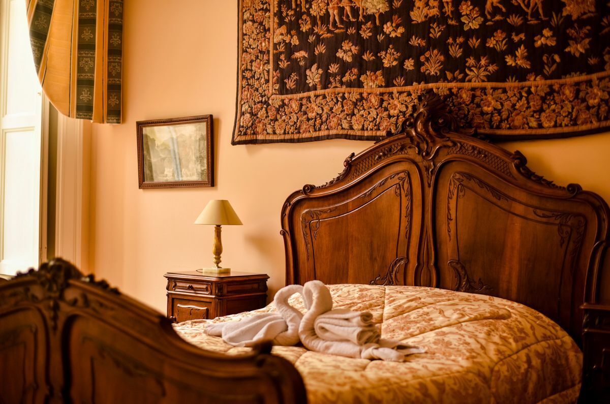 A bedroom with a wooden headboard, a bed with a floral bedspread, a nightstand with a lamp, and a tapestry on the wall.