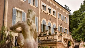 Un bâtiment imposant, doté d’une entrée monumentale, d’un escalier et d’une statue en premier plan.