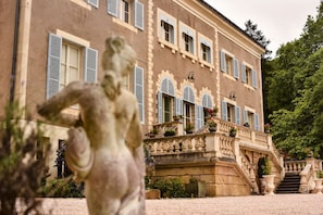 Un bĂątiment imposant, dotĂ© dâune entrĂ©e monumentale, dâun escalier et dâune statue en premier plan.