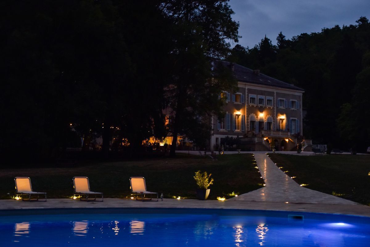 Una casa grande con piscina, mobiliario exterior y un camino iluminado que lleva a la entrada.