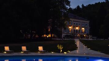 A large house with a swimming pool, outdoor seating, and a well-lit pathway leading to the entrance.