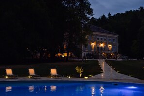 Un'ampia casa con piscina, area salotto esterna e un vialetto illuminato che conduce all'ingresso.