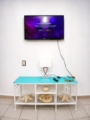 A television on a wall with a Wi-Fi setup, a white table with a teal top, and a lamp.
