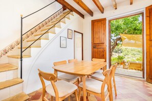 Un comedor con mesa y sillas de madera, una escalera con diseño floral y vistas por una puerta abierta.