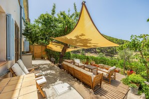 Un patio exterior con muebles de madera, una vela de sombra y vistas de la vegetación circundante.