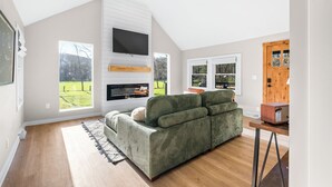 Una sala de estar moderna con un sofá grande de color verde, una chimenea y un televisor montado en la pared.