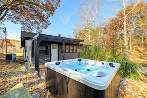 A hot tub in a backyard with a wooden deck, a small shed, and autumn foliage.