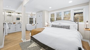 Un dormitorio con cama, mesitas de noche, cómoda, espejo y ventana.