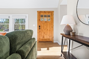 En trædør, en grøn sofa, en lampe og et rundt spejl på væggen.