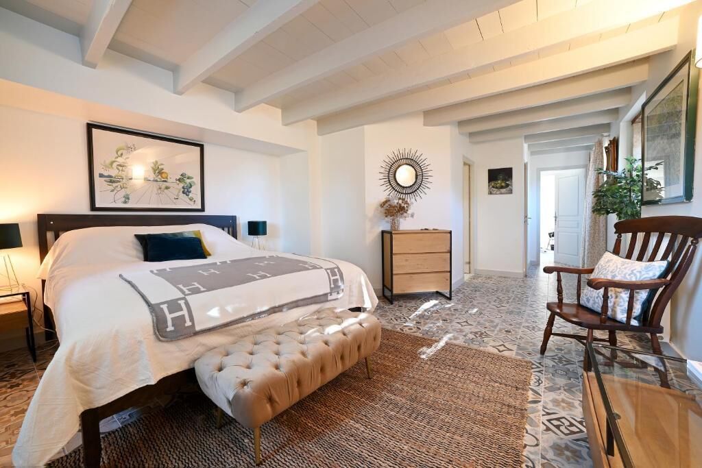 Un dormitorio con cama, mesitas de noche, una silla, un espejo y una alfombra.