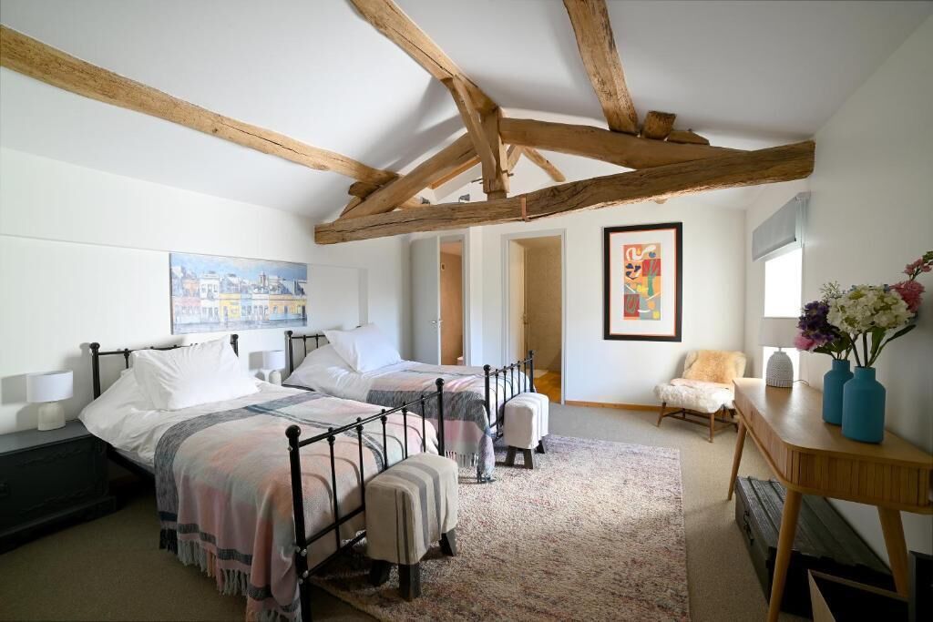 Un dormitorio con dos camas, techo de madera, un cuadro, una silla y un escritorio con un jarrón.