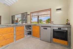 Eine Küche mit eingebautem Bosch Geschirrspüler, einem Bosch Backofen, Holzausbau und einem großen Fenster mit Blick ins Freie.