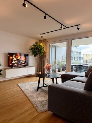 A modern living room with a flat-screen TV, a sofa, a coffee table, and a potted plant.