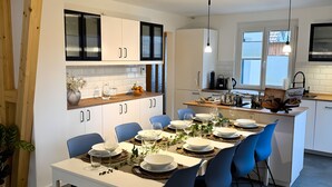 Een moderne keuken met witte kasten, een eethoek met blauwe stoelen en een centraal keukenblok met spoelbak en fornuis.