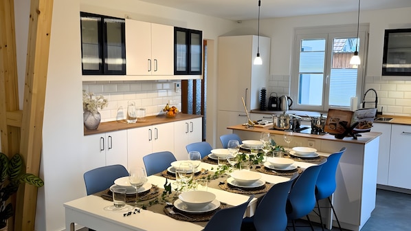 A modern kitchen with white cabinets, a dining area with blue chairs, and a central island with a sink and stove.