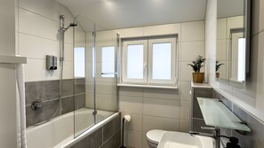 A modern bathroom with a glass-enclosed shower, a bathtub, a toilet, and a vanity with a mirror.