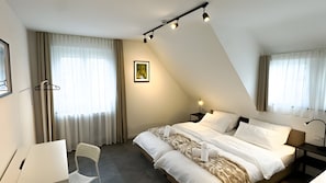 A modern hotel room with a bed, a chair, a desk, and a picture on the wall.