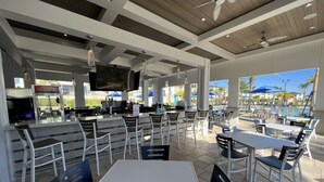 Un espace extérieur aménagé pour les repas, avec des tables et des chaises, un bar et une piscine en arrière-plan.