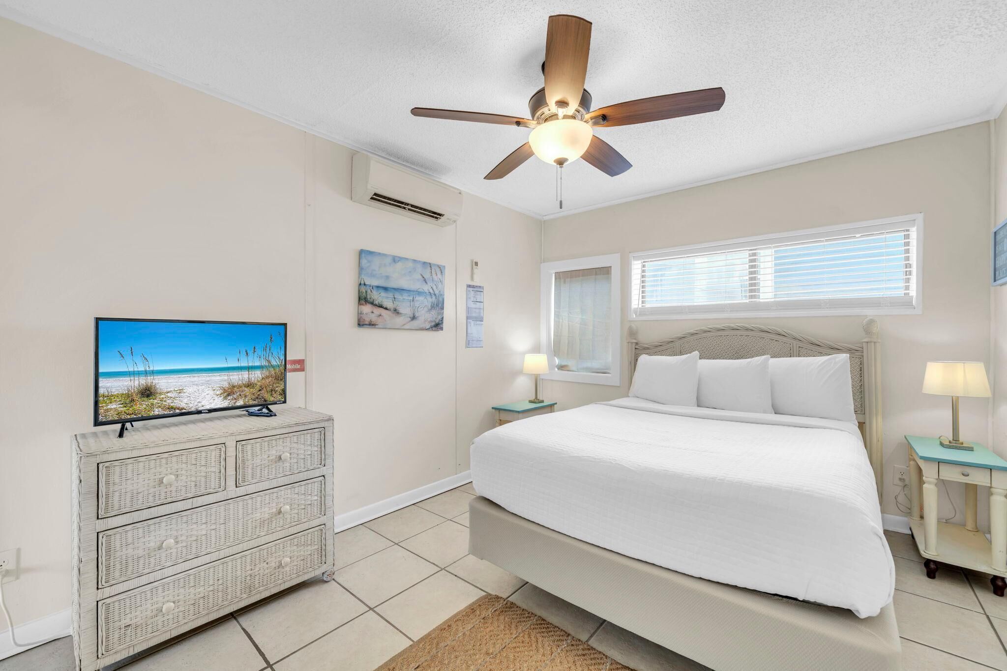 Quarto com cama, ventoinha no teto, televisão, cômoda e janela com persianas.