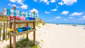 Un letrero de madera con la inscripción 'Beach Toys' y 'take some - leave some', ubicado en una playa con una cerca de madera y un paseo de madera que conduce a la playa.