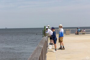 Eine Pier mit Menschen beim Angeln, einem hölzernen Geländer und einem ruhigen Meer im Hintergrund.