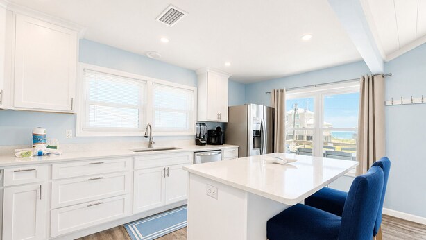 Una cocina moderna con armarios blancos, una isla central, una cafetera y un refrigerador.