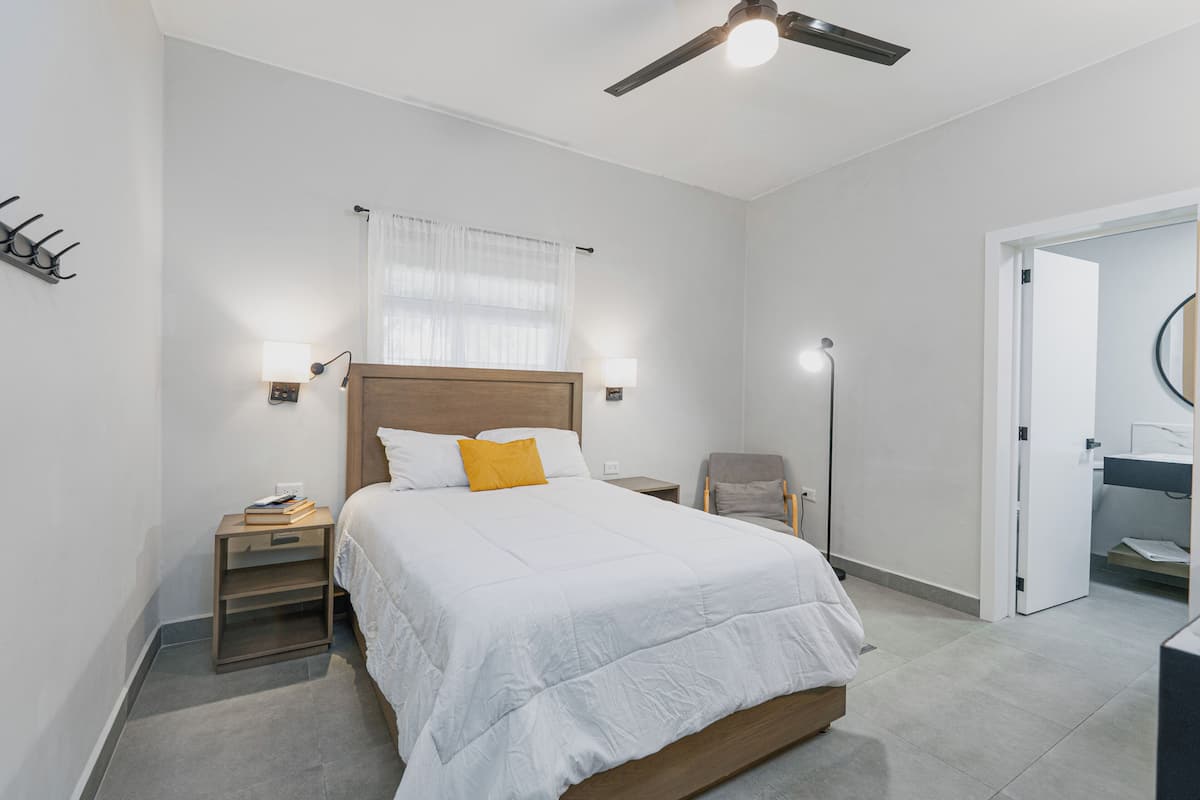 A bedroom with a bed, bedside tables, a chair, a ceiling fan, and a door leading to a bathroom.