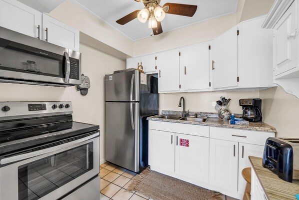 A kitchen with a microwave, oven, refrigerator, and a ceiling fan. - Linda's Cozy Cottage A (Panama City Beach)